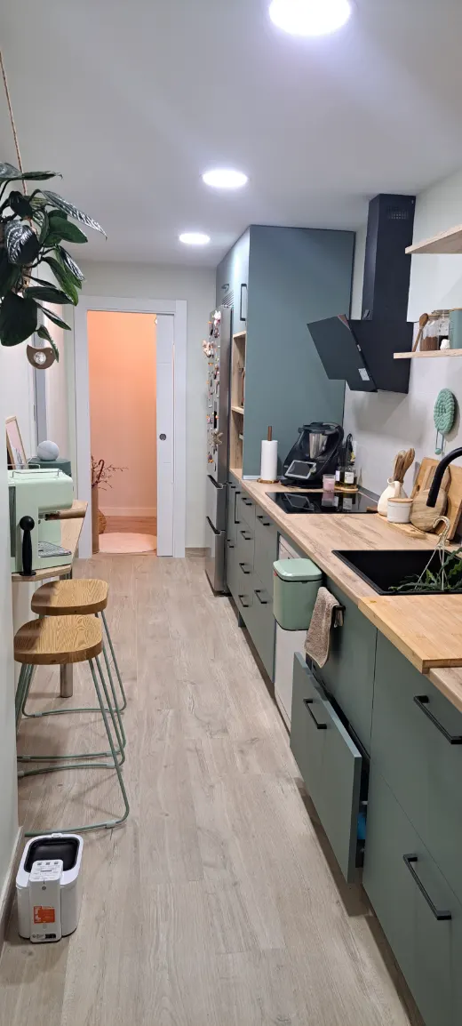 Cocina lineal con muebles verdes, encimera de madera y campana negra